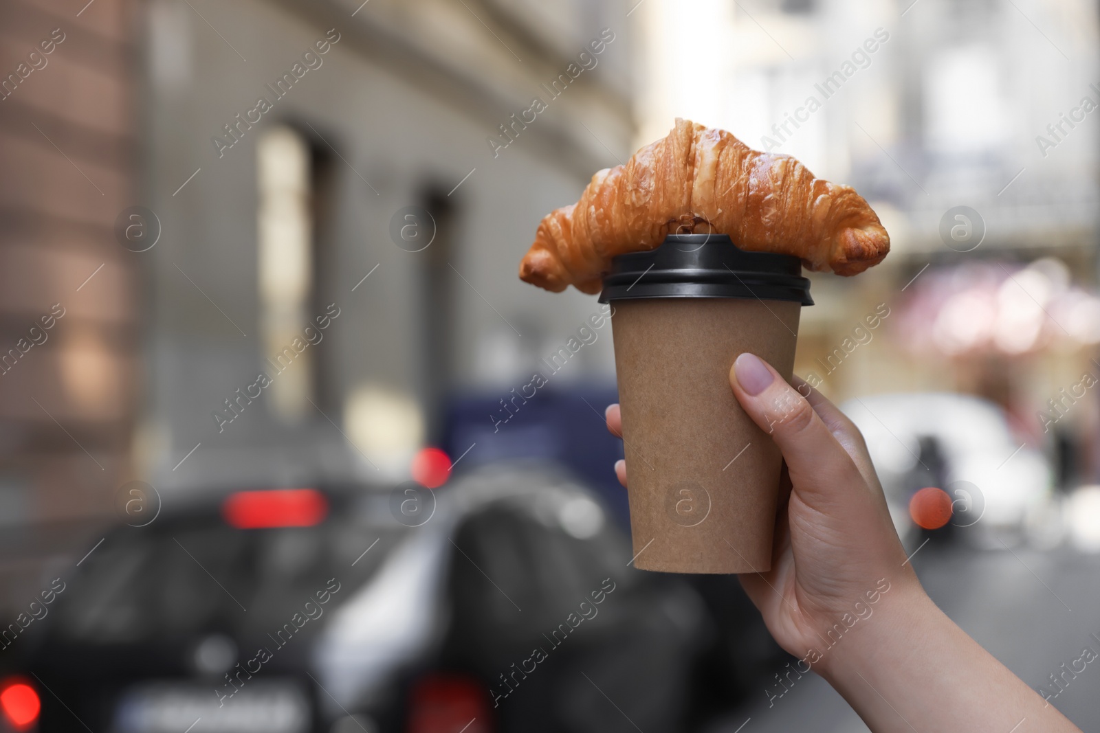 Photo of Woman holding tasty croissant and cup of coffee on city street, closeup. Space for text