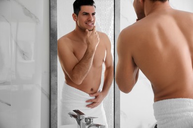 Handsome man touching his smooth face after shaving near mirror in bathroom