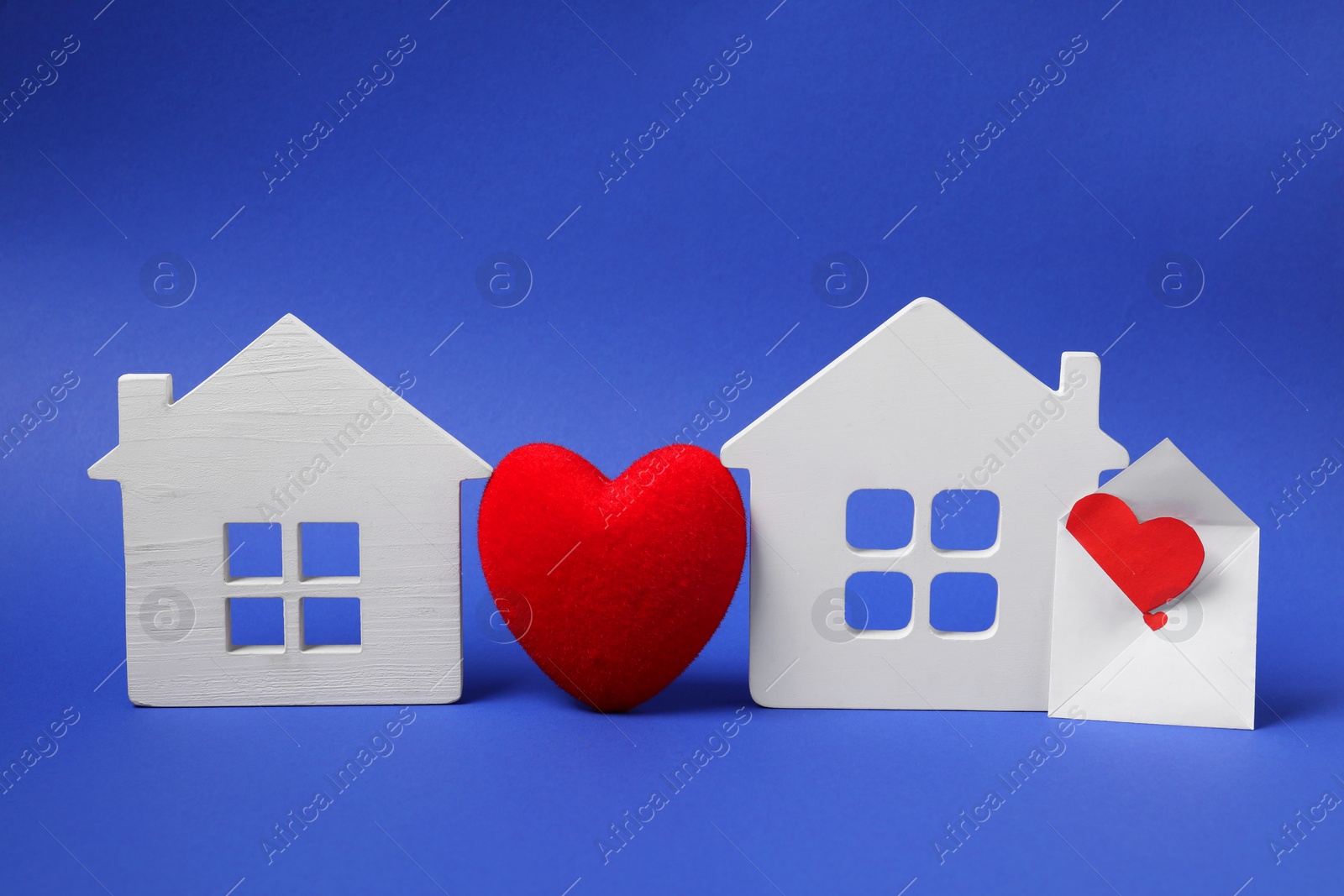 Photo of Long-distance relationship concept. Decorative heart between two white house models and love letter on blue background