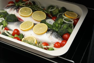 Photo of Raw fish with vegetables and lemon in baking dish into oven