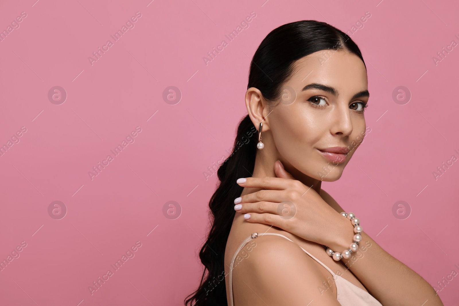 Photo of Young woman wearing elegant pearl jewelry on pink background, space for text