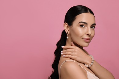 Young woman wearing elegant pearl jewelry on pink background, space for text