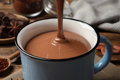 Photo of Pouring yummy hot chocolate into mug on table, closeup