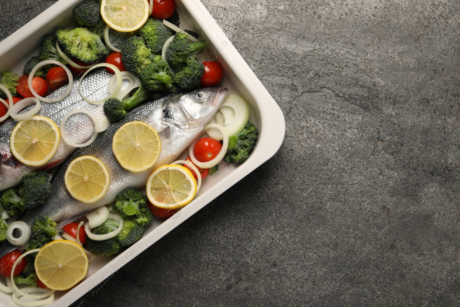 Photo of Raw fish with vegetables and lemon in baking dish on grey textured table, top view. Space for text