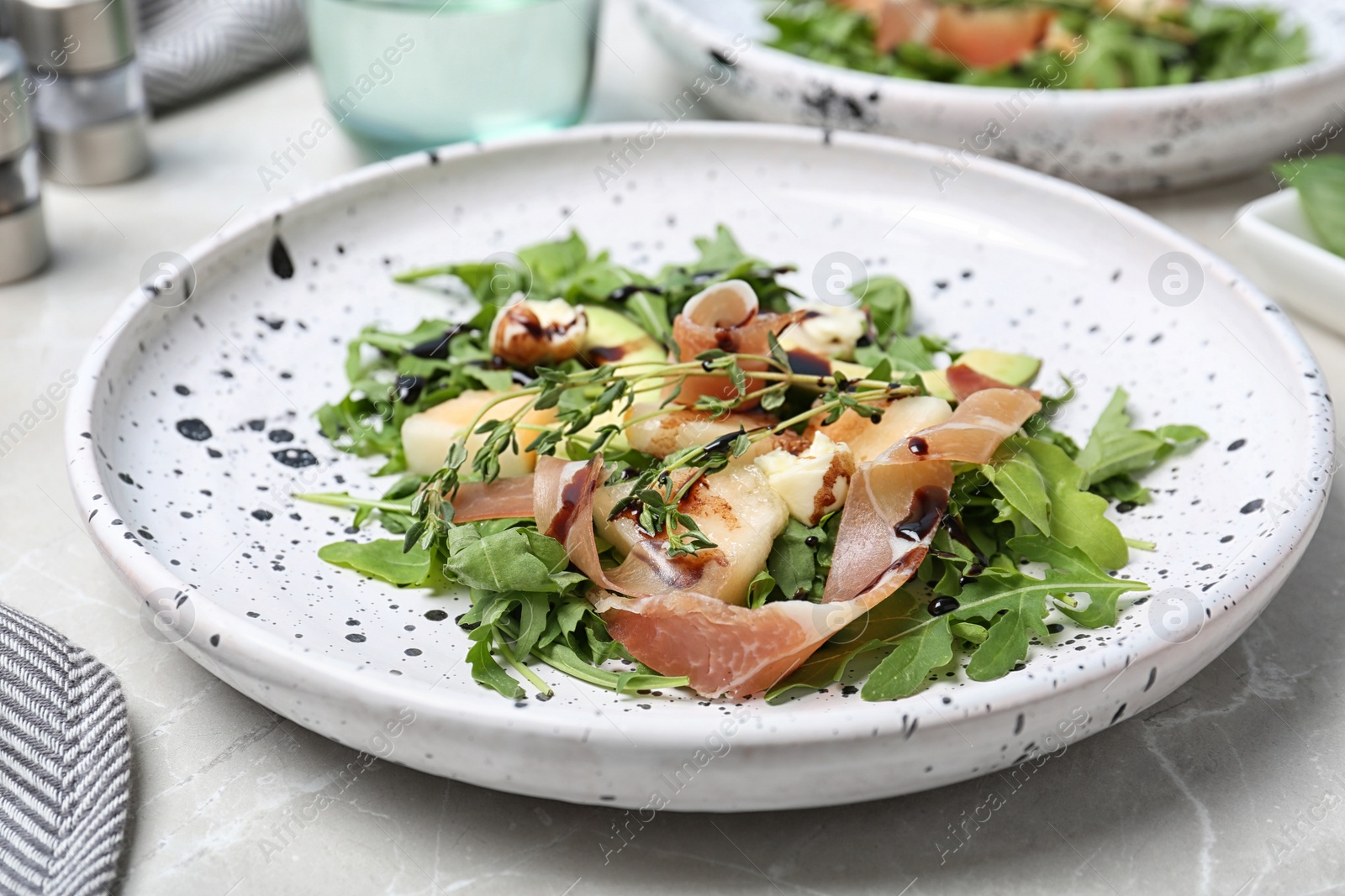 Photo of Plate of salad with melon slices and prosciutto on gray table