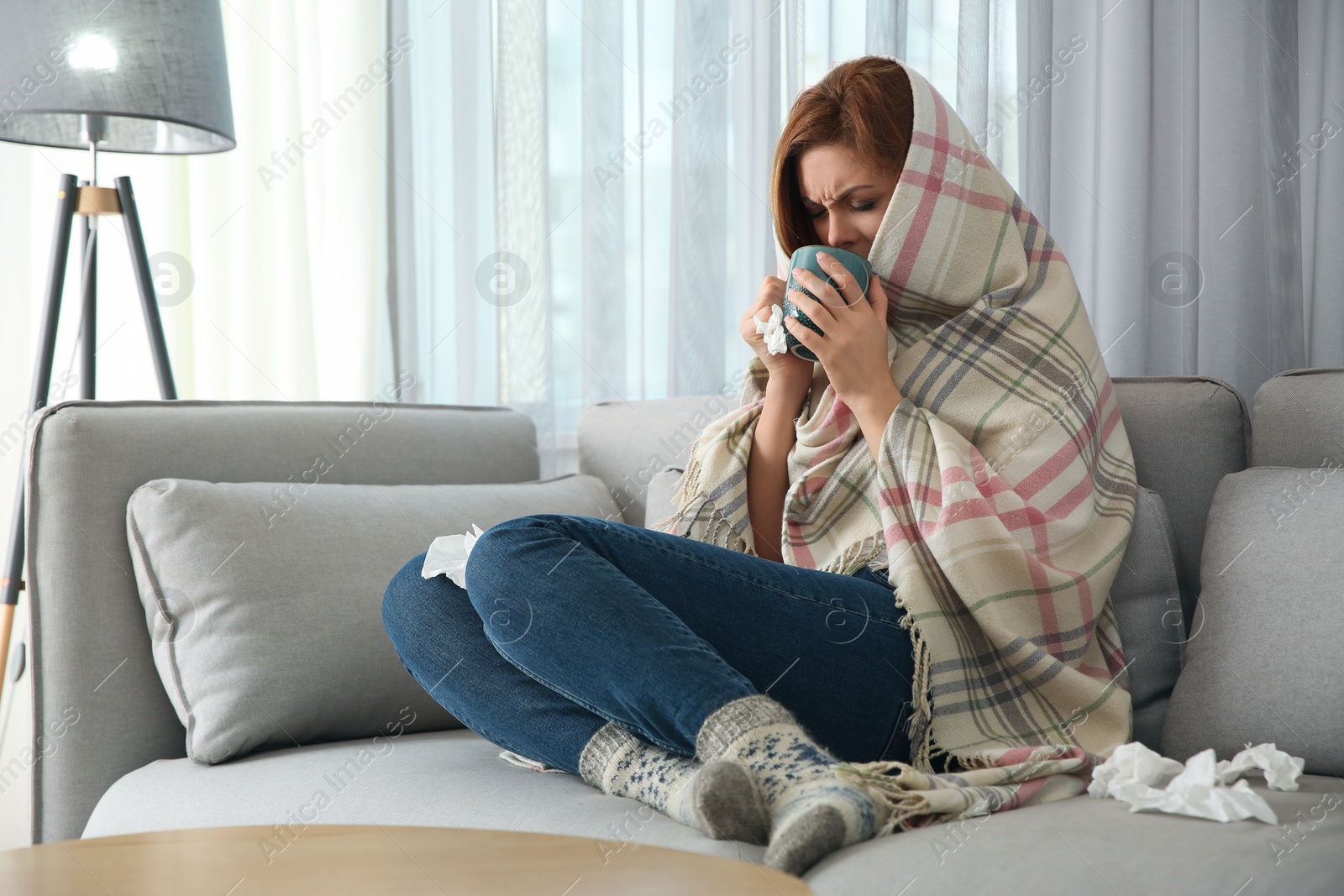 Photo of Sick woman wrapped in plaid with cup of hot drink at home. Influenza virus