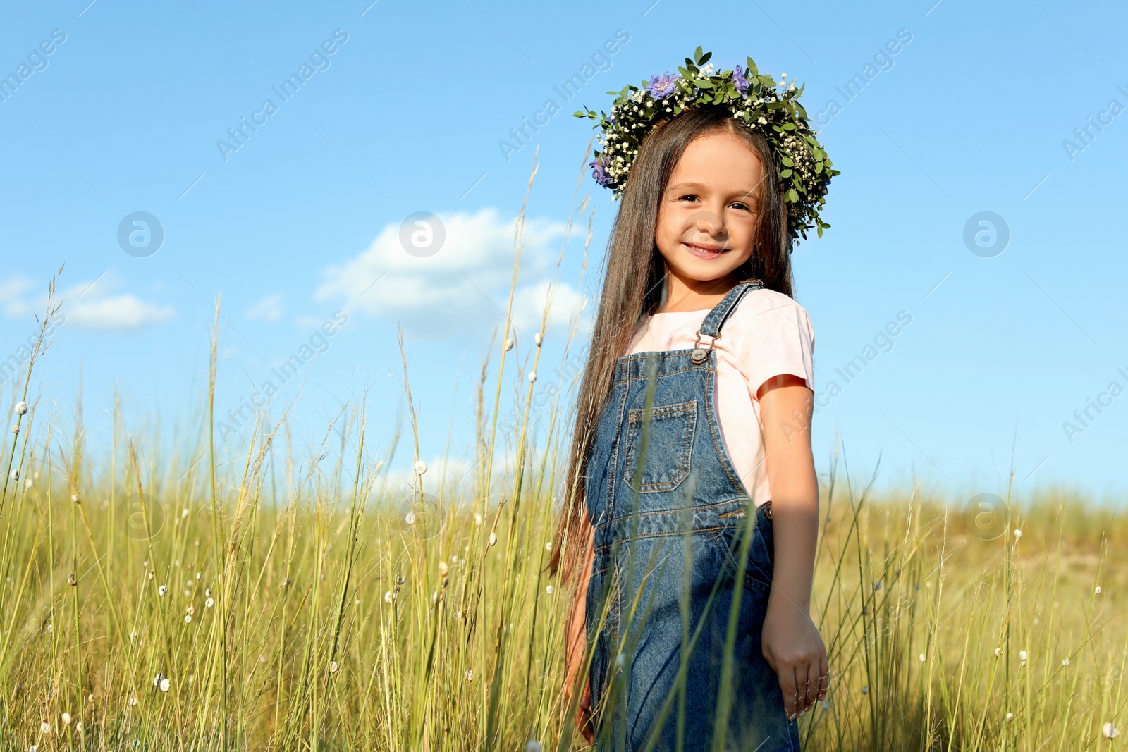 Photo of Cute little girl wearing flower wreath outdoors, space for text. Child spending time in nature