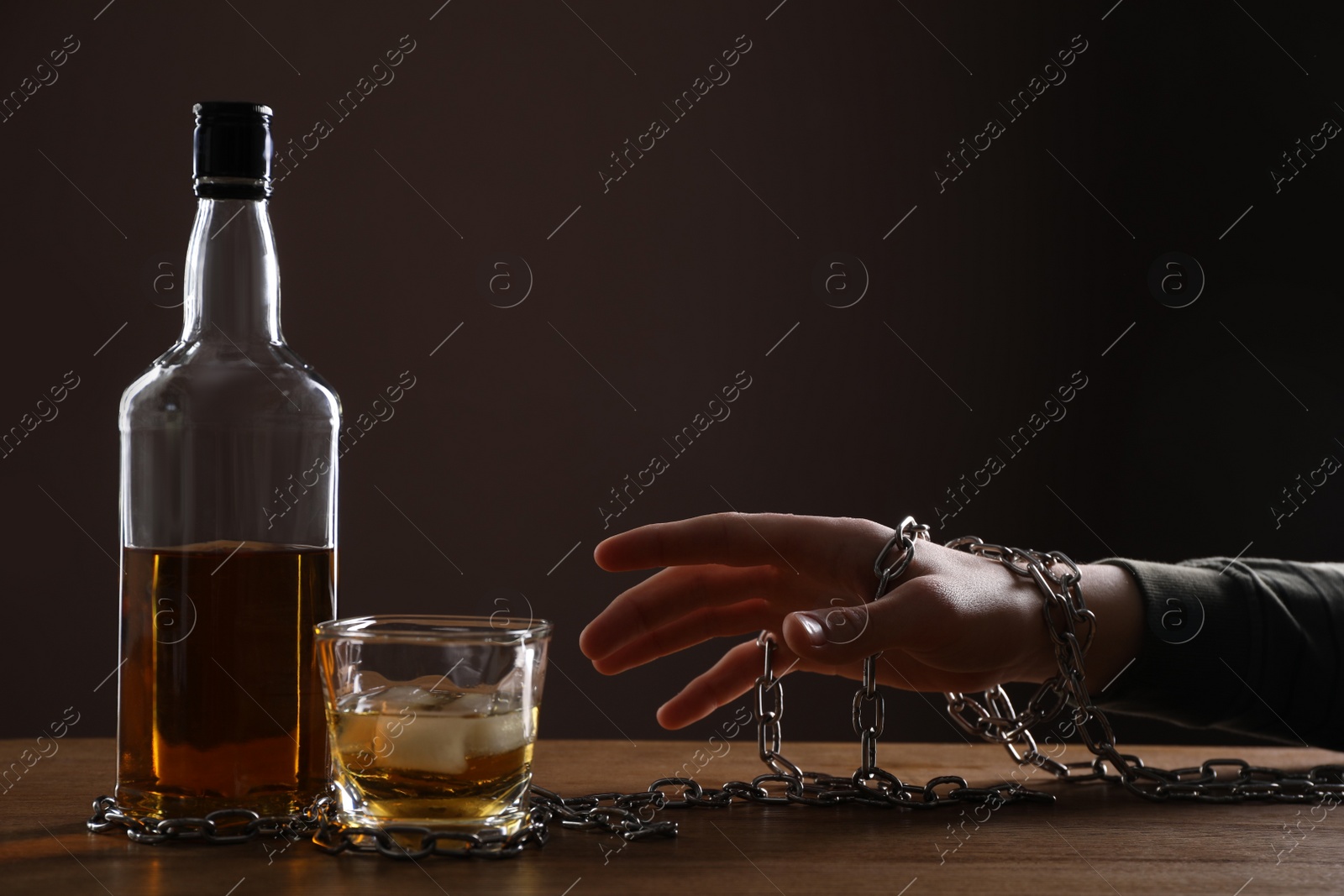 Photo of Alcohol addiction. Man chained with bottle of whiskey at wooden table, closeup