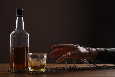 Alcohol addiction. Man chained with bottle of whiskey at wooden table, closeup