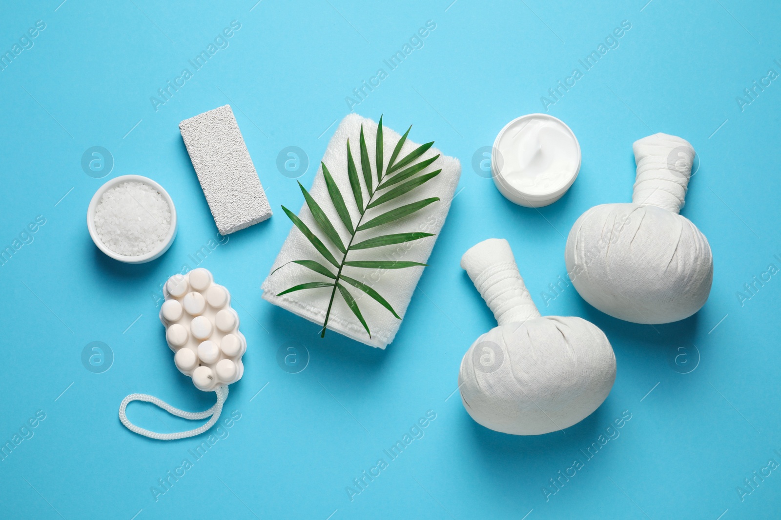 Photo of Beautiful spa composition with herbal massage bags and different care products on light blue background, flat lay