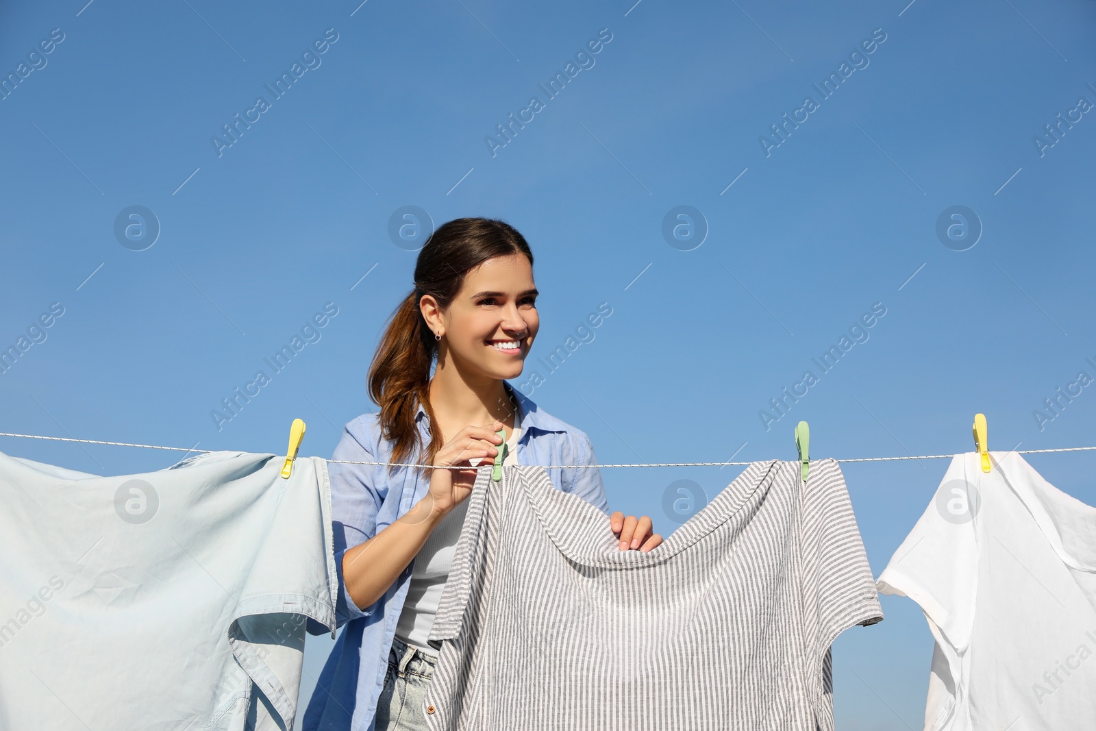 Photo of Woman hanging clothes with clothespins on washing line for drying against blue sky