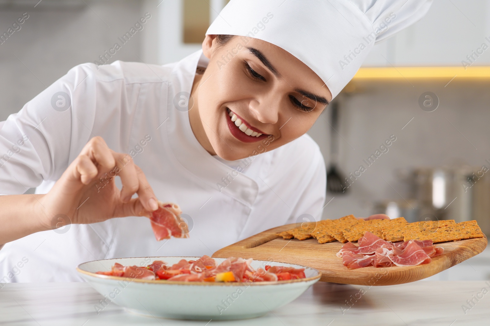 Photo of Professional chef adding prosciutto into delicious dish at white marble table in kitchen