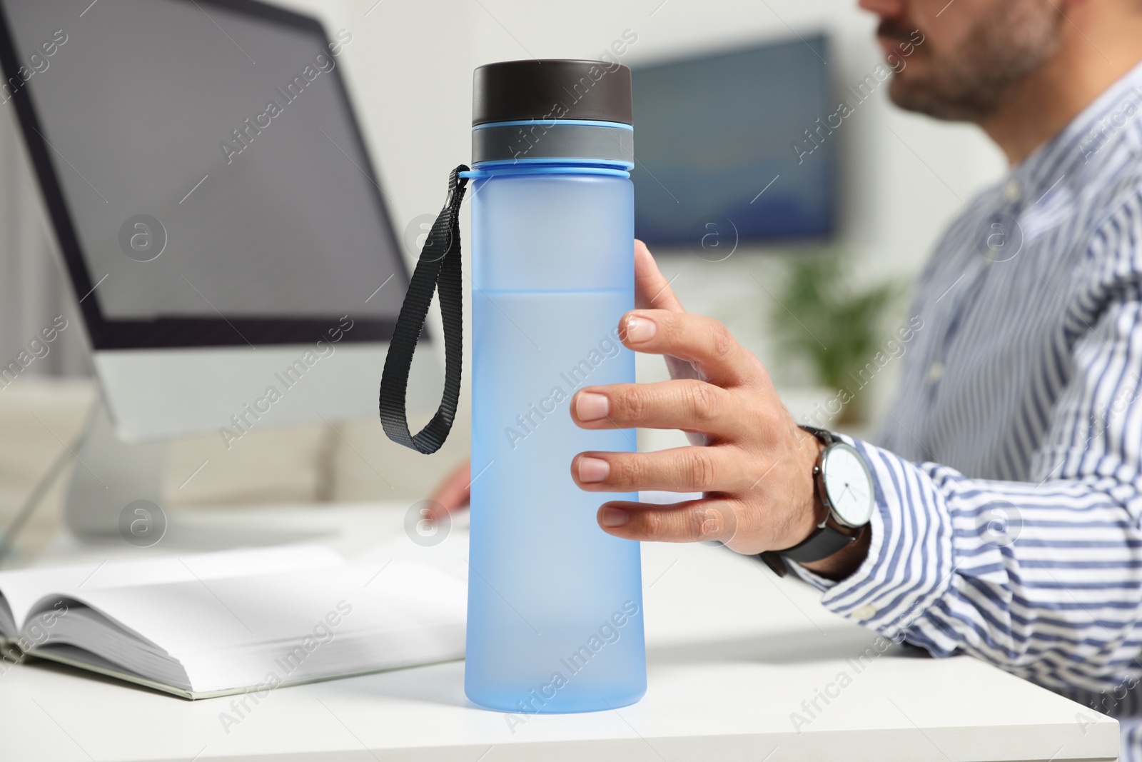 Photo of Man taking transparent plastic bottle of water while working on computer in office, closeup