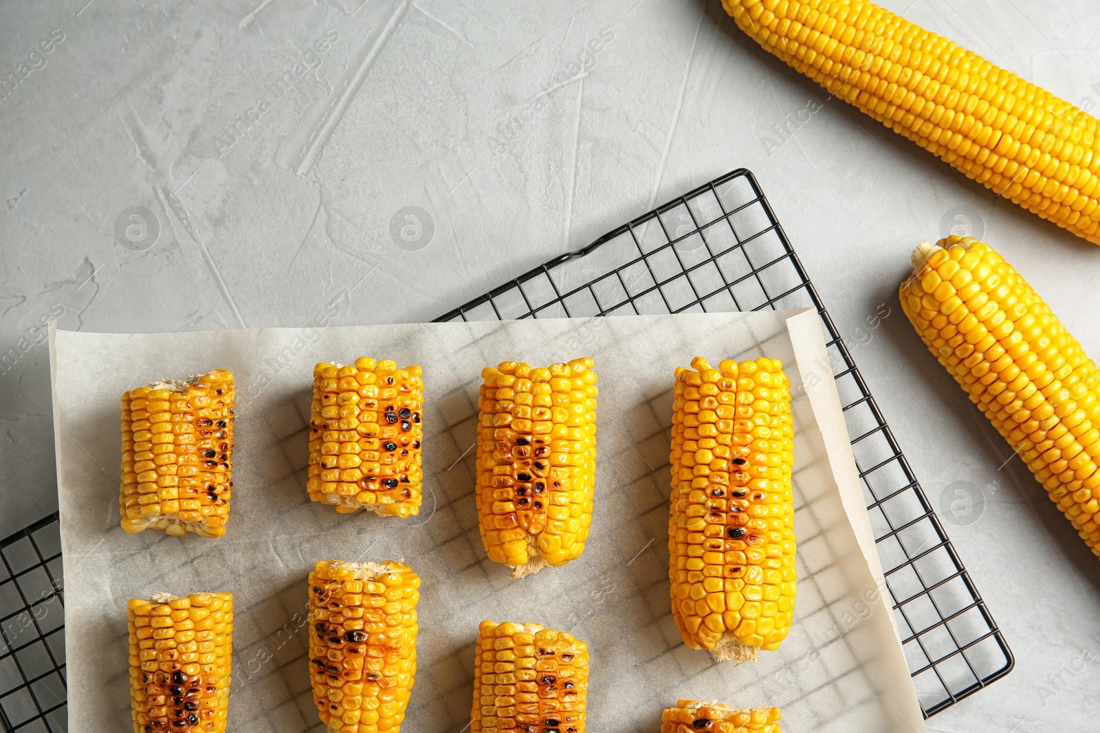 Photo of Cooling rack with grilled corn cobs on light background, top view