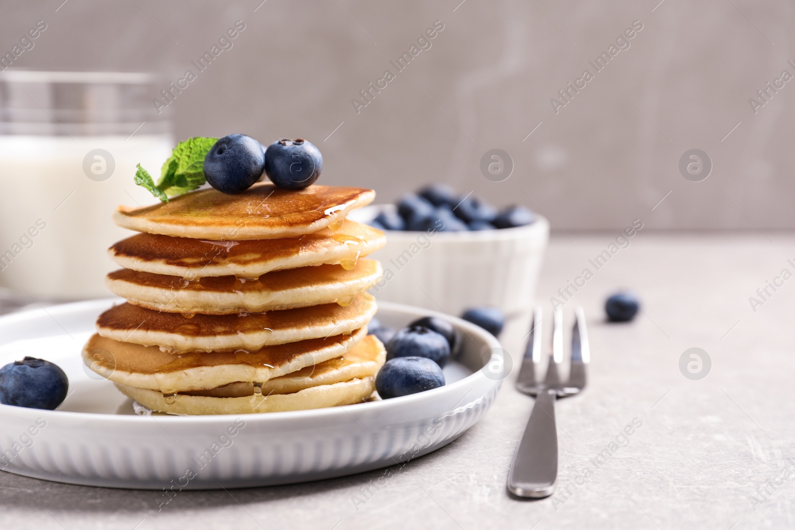 Photo of Plate of tasty pancakes with blueberries and honey on light grey table. Space for text