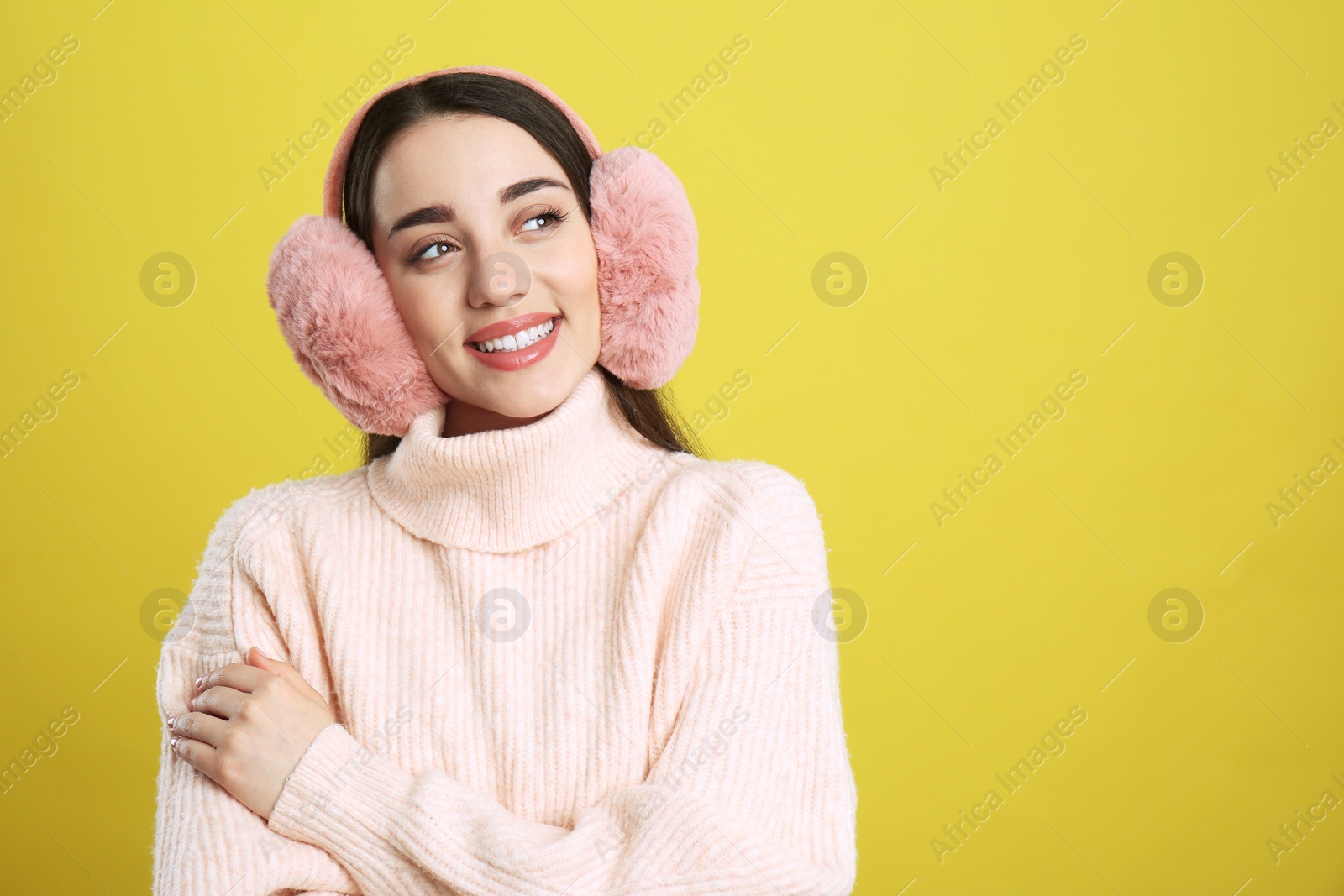 Photo of Beautiful young woman wearing earmuffs on yellow background. Space for text