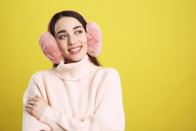 Photo of Beautiful young woman wearing earmuffs on yellow background. Space for text