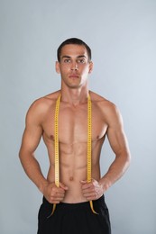 Photo of Handsome shirtless man with slim body and measuring tape on grey background