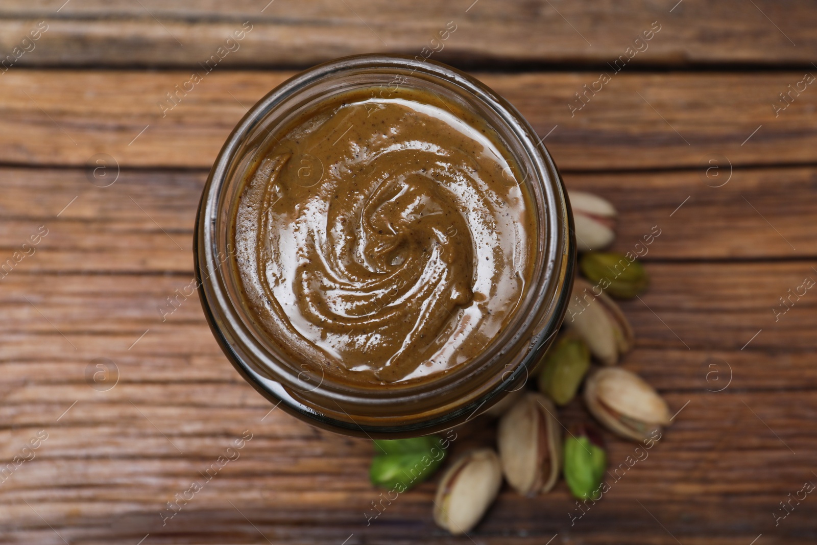 Photo of Tasty pistachio nut paste in jar on wooden table, top view