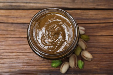 Tasty pistachio nut paste in jar on wooden table, top view