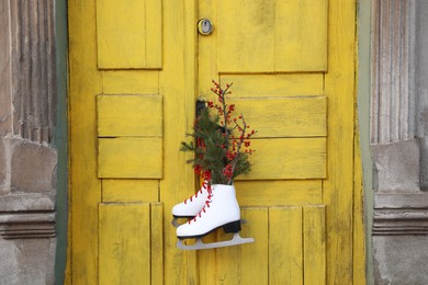Photo of Pair of ice skates with Christmas decor hanging on old yellow door