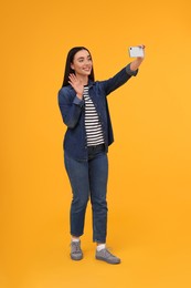 Photo of Smiling young woman taking selfie with smartphone on yellow background