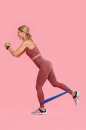 Woman exercising with elastic resistance band on pink background