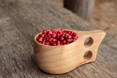 Cup with tasty ripe lingonberries on wooden table, space for text