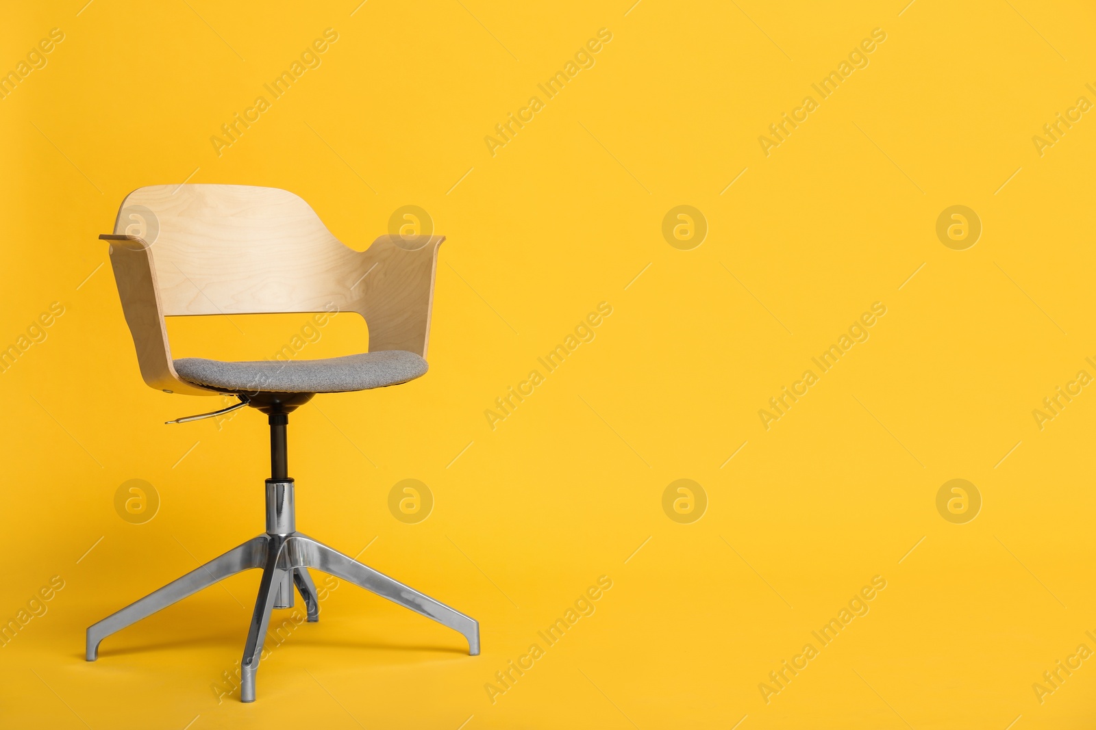 Photo of Modern office chair on yellow background. Space for text