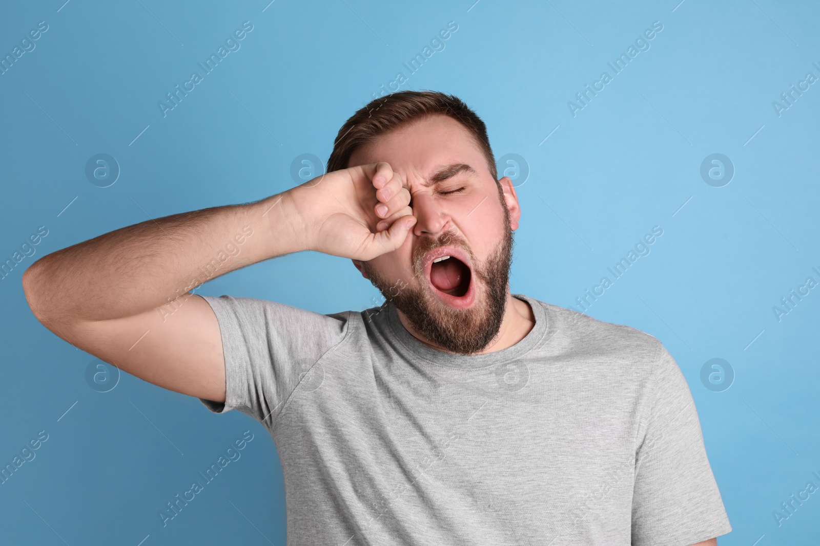 Photo of Sleepy young man yawning on light blue background