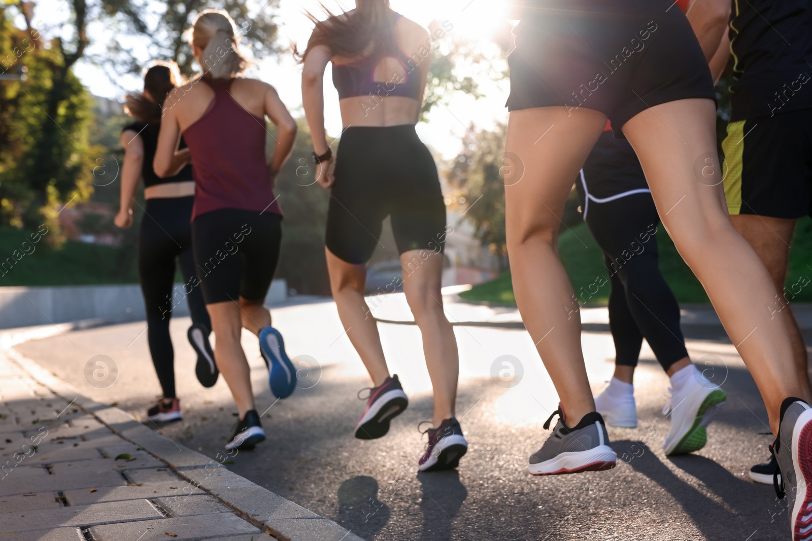 Photo of Group of people running outdoors on sunny day, back view