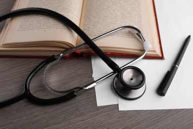 Book, stethoscope, pen and paper on wooden table. Medical education