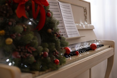 White piano with festive decor and note sheets indoors, closeup. Christmas music