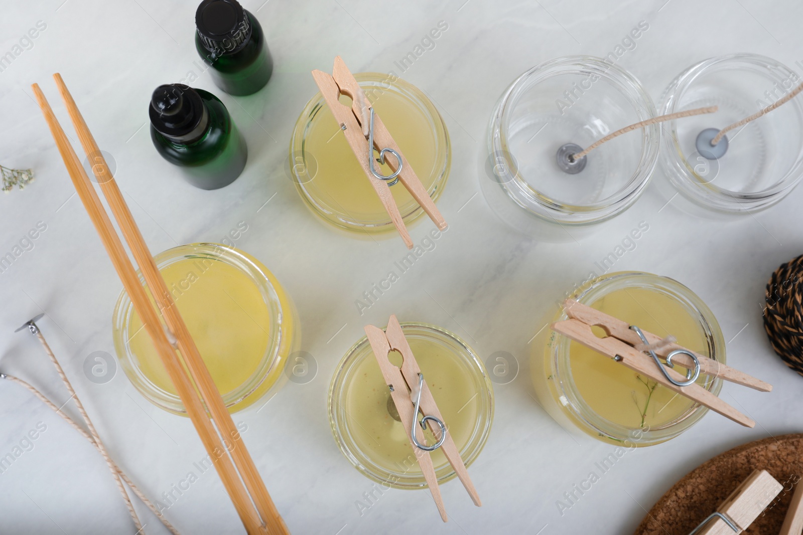 Photo of Glass jars with melted wax on white table, flat lay. Handmade candles