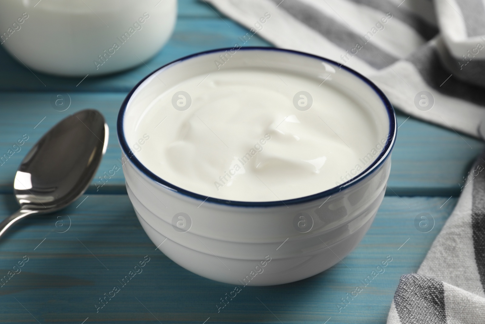 Photo of Bowl of tasty yogurt on light blue wooden table