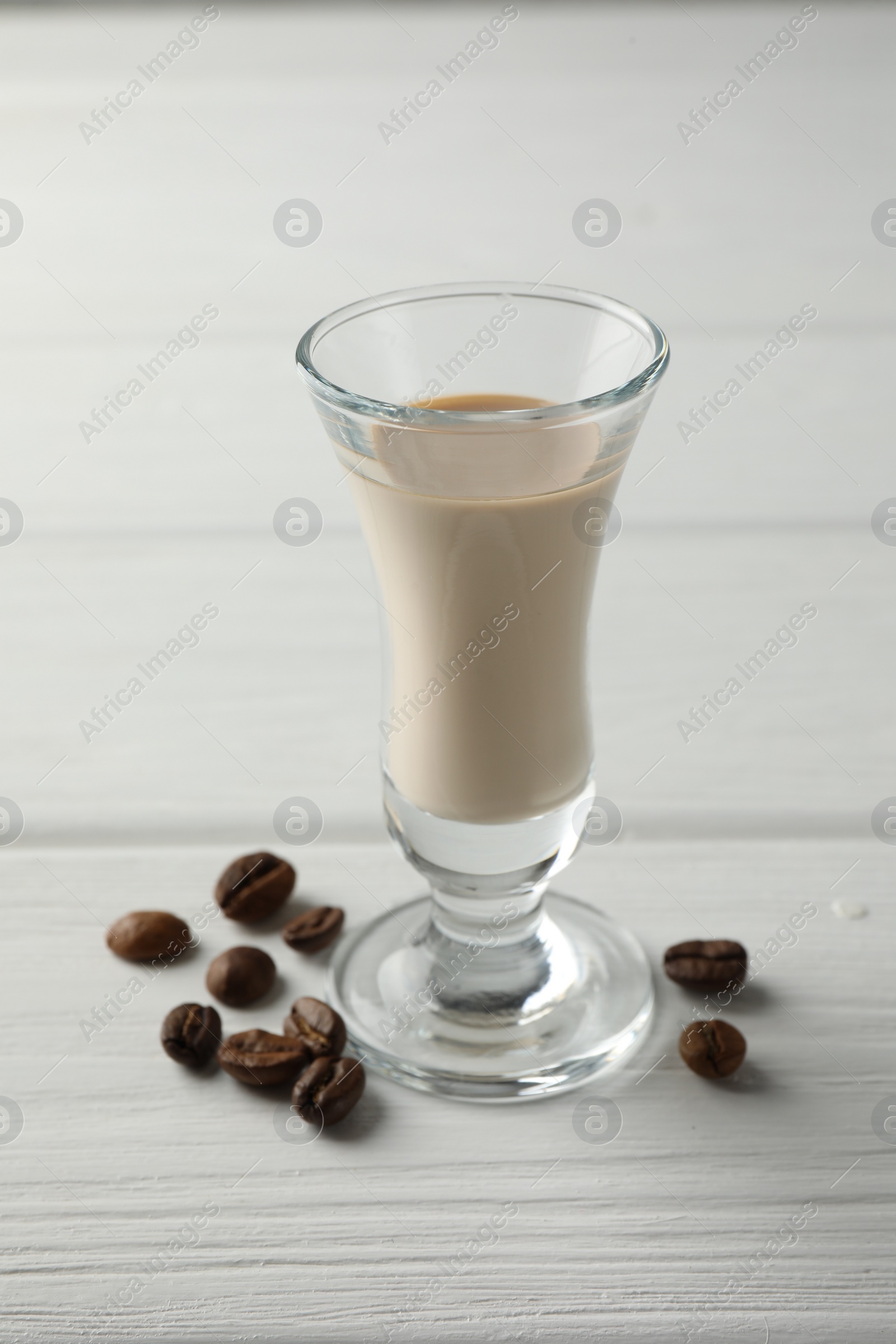 Photo of Coffee cream liqueur in glass and beans on white wooden table