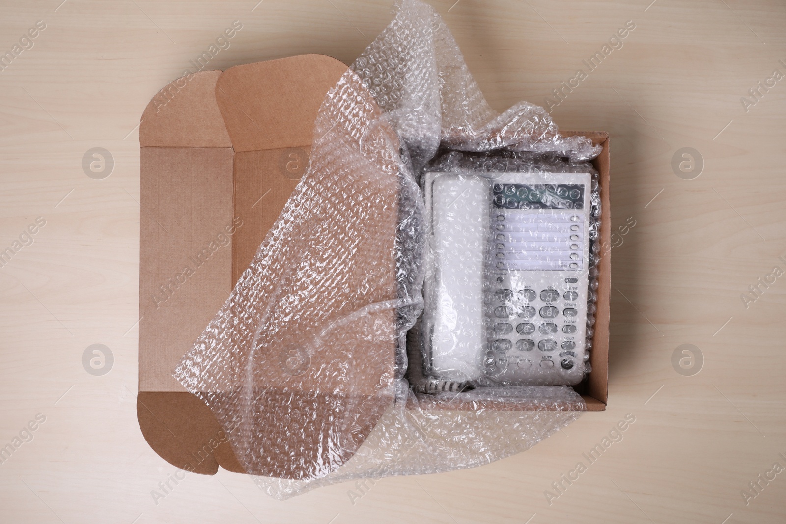 Photo of Corded phone with bubble wrap in cardboard box on wooden table, top view