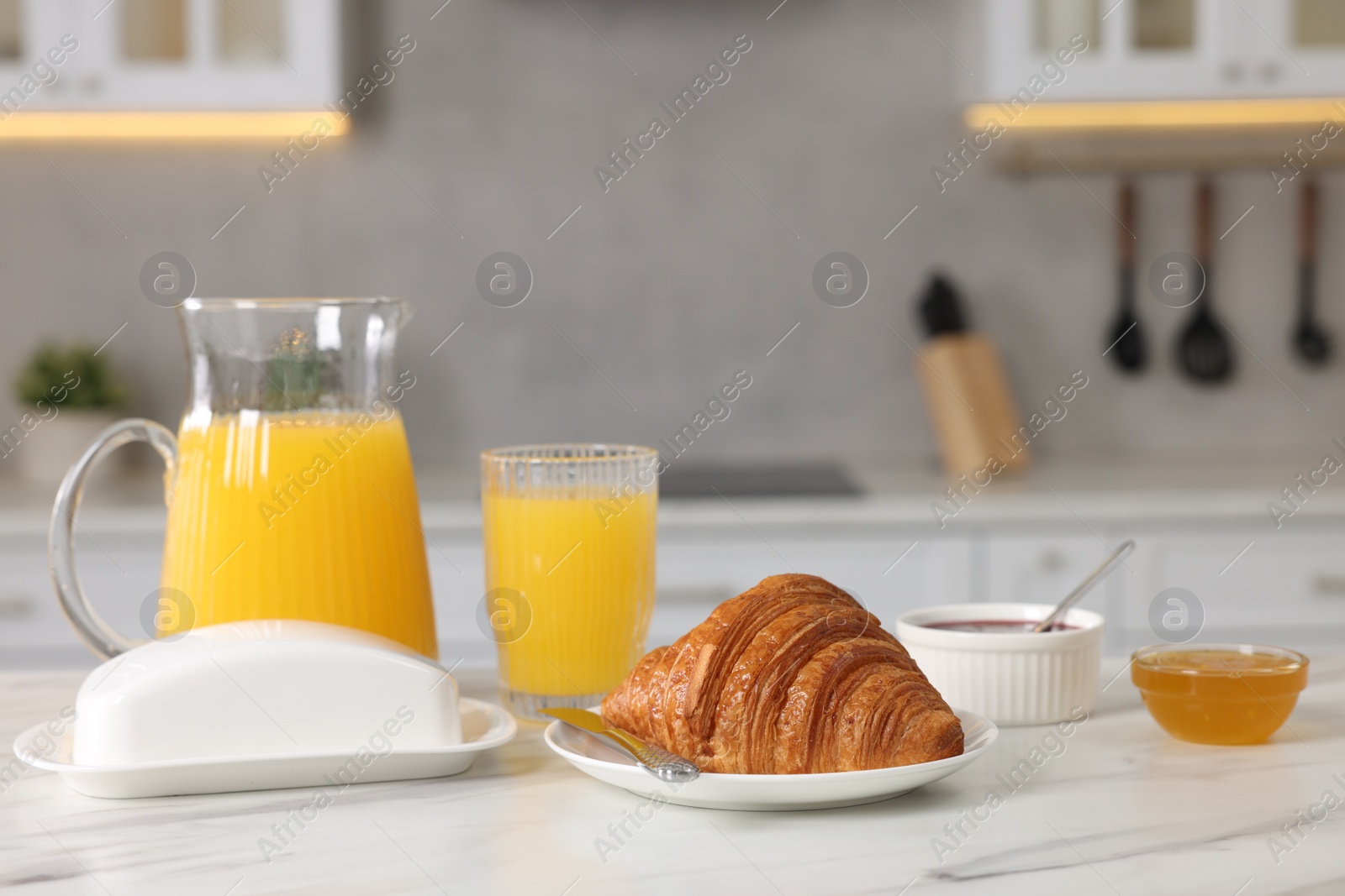 Photo of Breakfast served in kitchen. Fresh croissant, jam, honey and orange juice on white table