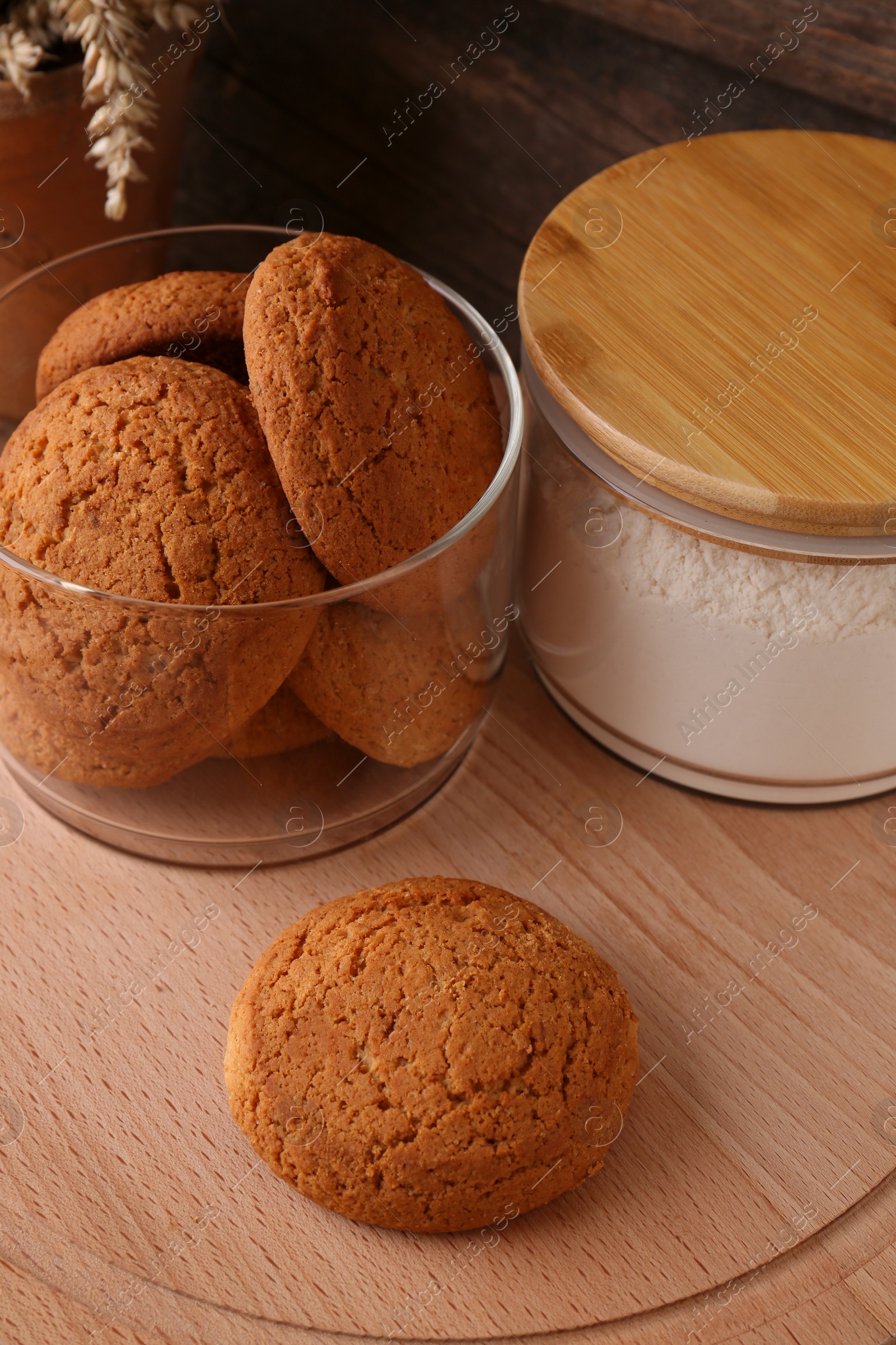 Photo of Cookies and jar of wheat flour on wooden board, closeup view