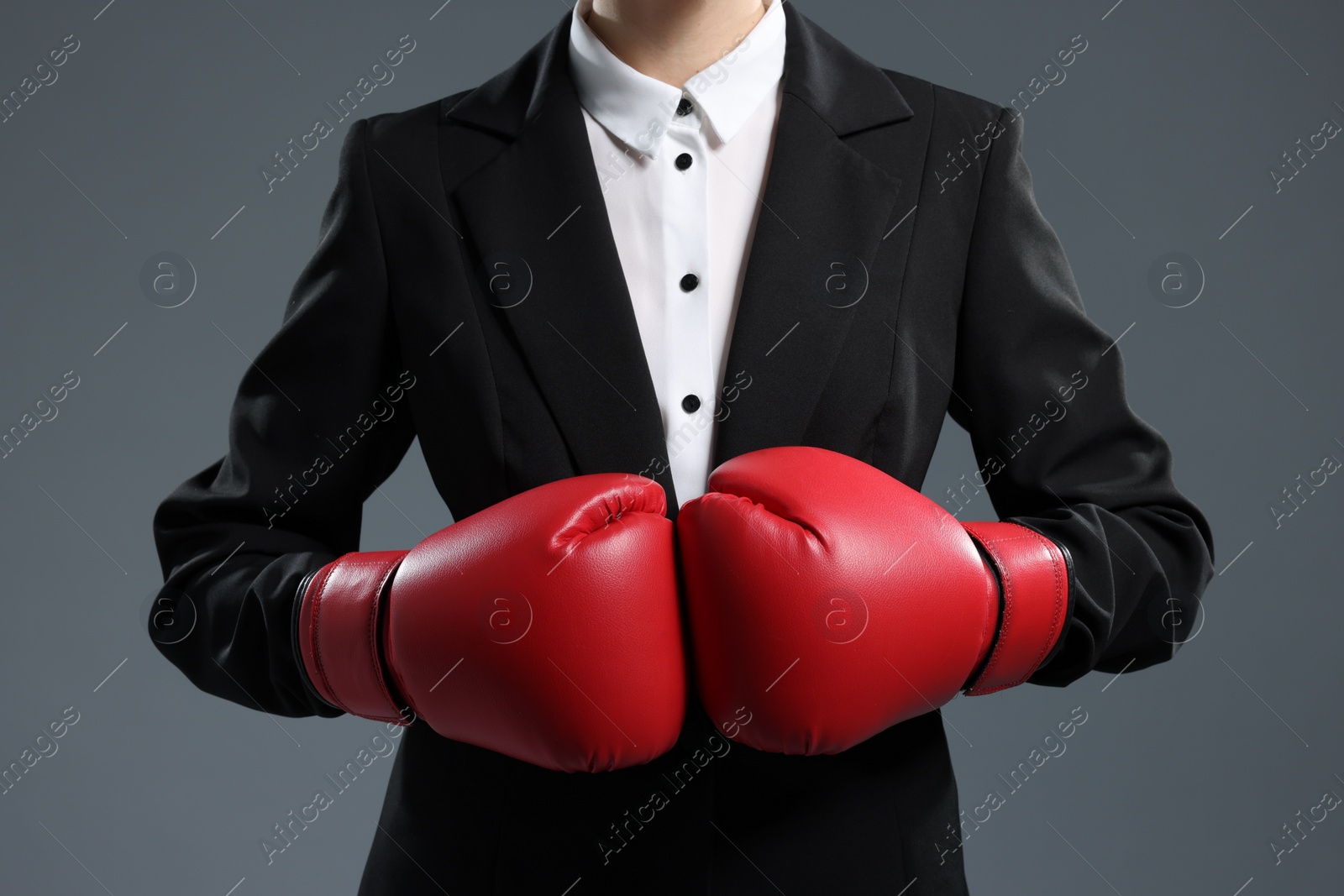 Photo of Businesswoman in suit wearing boxing gloves on grey background, closeup