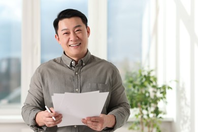 Photo of Portrait of smiling businessman with documents in office. Space for text