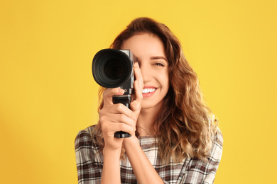 Photo of Beautiful young woman with vintage video camera on yellow background