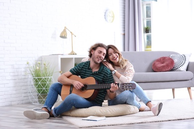 Photo of Young man playing acoustic guitar for his girlfriend in living room