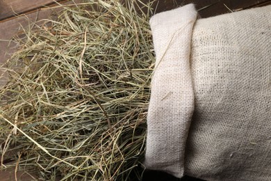 Dried hay in burlap sack on wooden table, top view