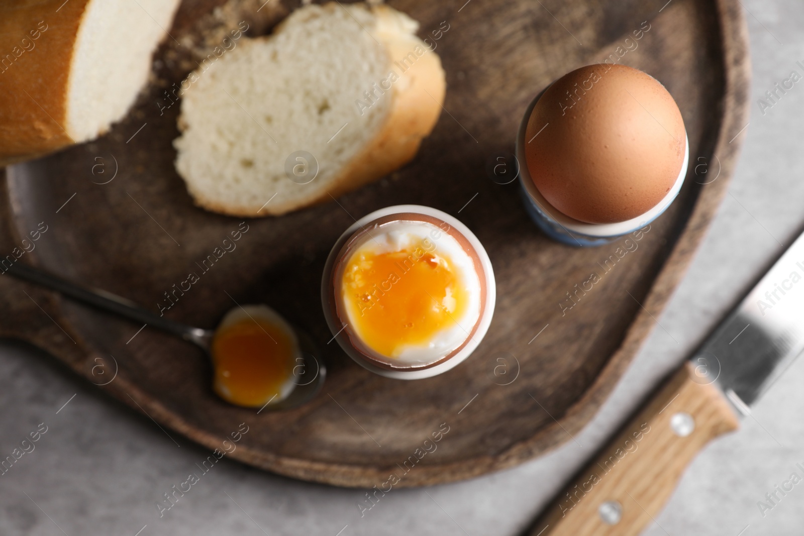 Photo of Fresh soft boiled eggs in cups and bread on grey table, flat lay