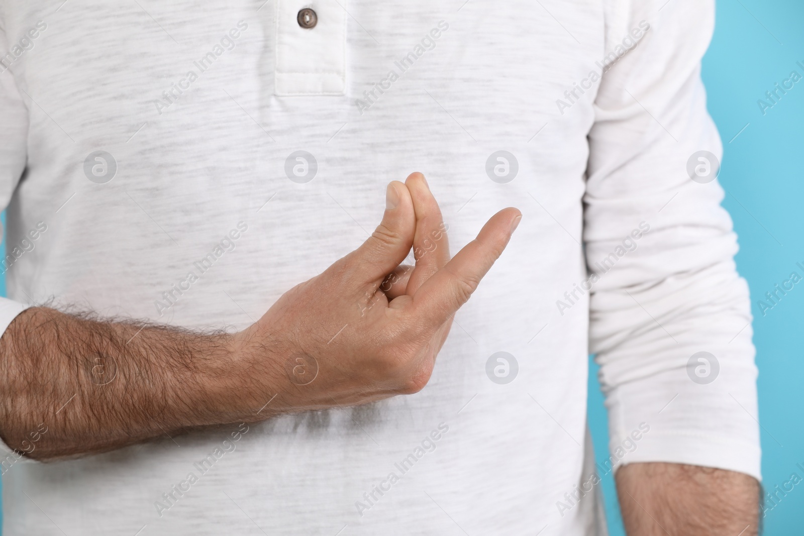 Photo of Man snapping his fingers on light blue background, closeup. Bad habit