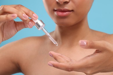 Photo of Woman applying serum onto her finger on light blue background, closeup