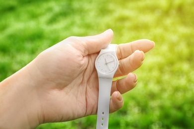 Woman holding beautiful wristwatch on blurred background, focus on hand. Time change concept