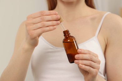 Photo of Woman with bottle of essential oil on blurred background, closeup