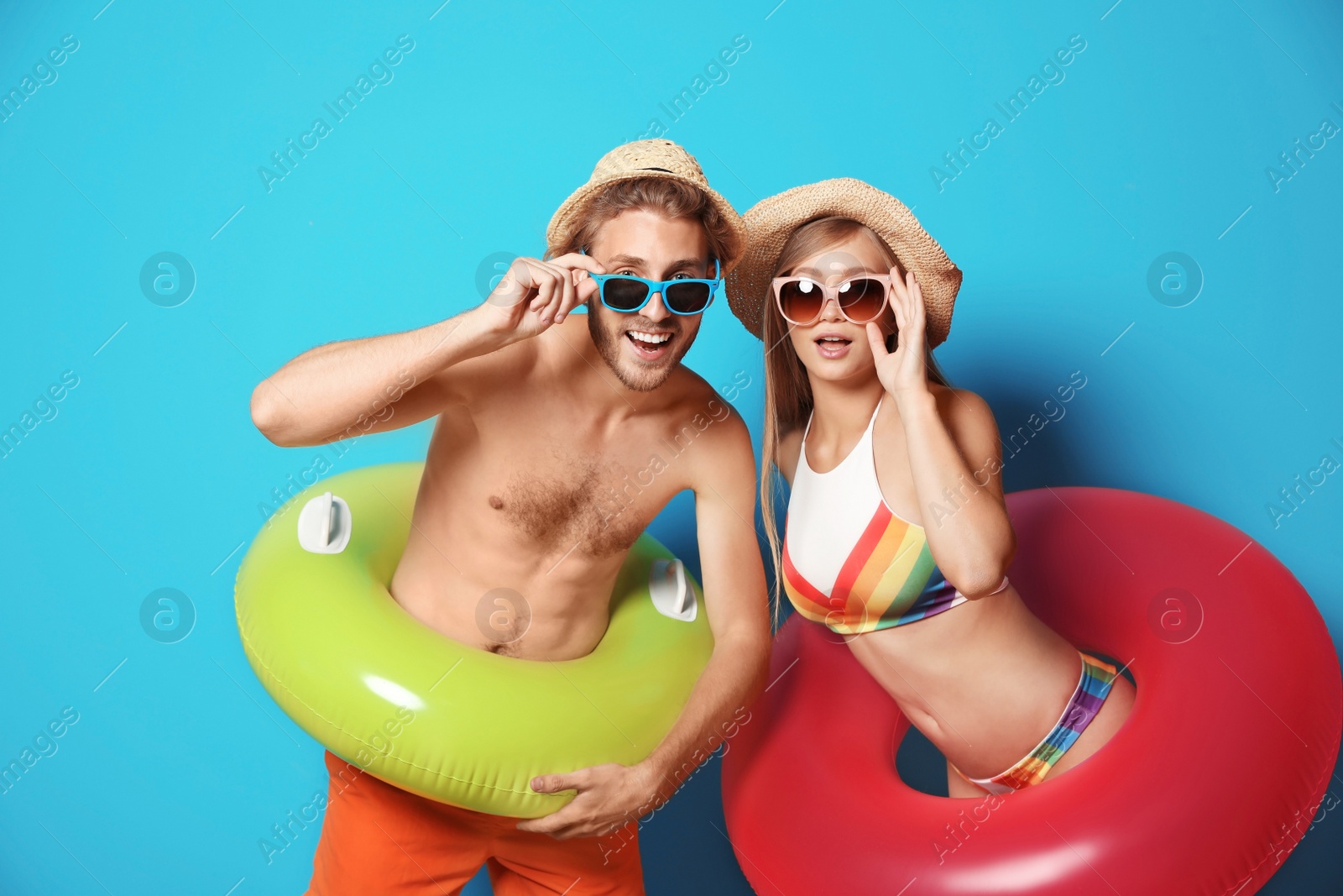 Photo of Young couple in beachwear with inflatable rings on color background